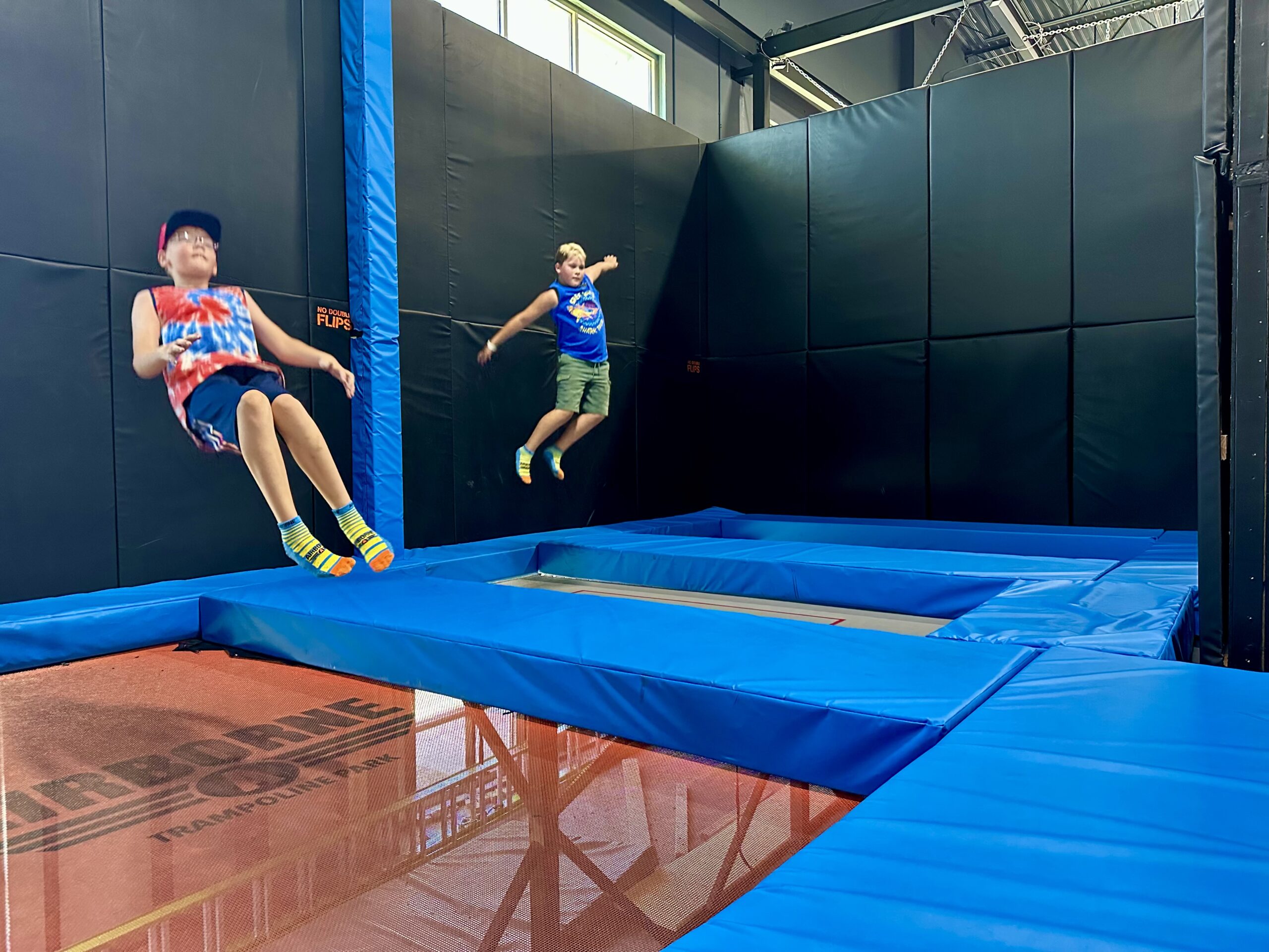 Two young boys bouncing on traTwo young boys bouncing on trampolines in an indoor trampoline park.mpolines in an indoor trampoline park.